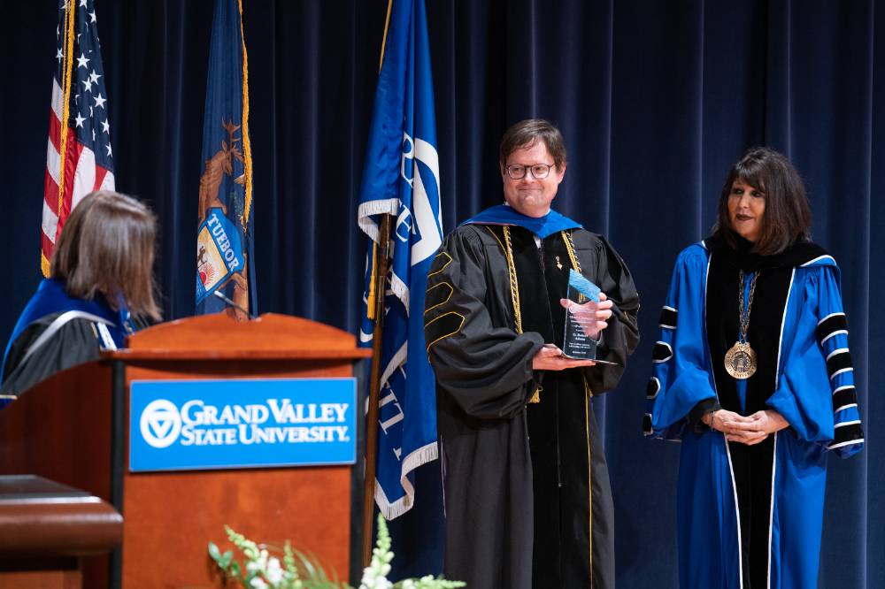 faculty member holds award smiling on stage